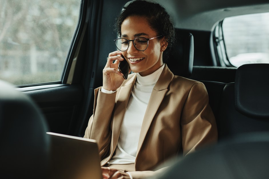 Businesswoman in a cab looking at her laptop while discussing business on the phone