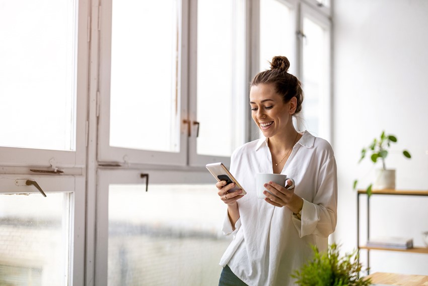 Smiling woman checking at the timesheet notifications using a smartphone while having coffee break