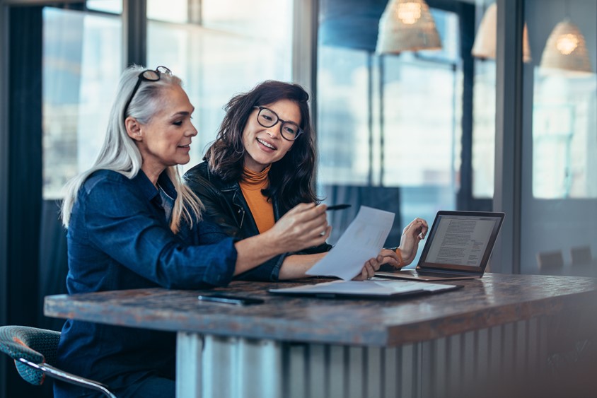 Two women working together to dicuss the printed page of reporting data