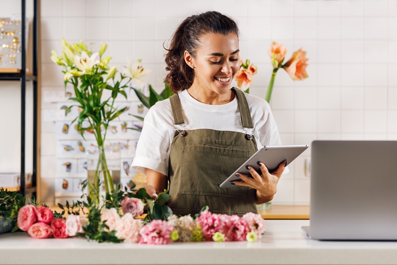A smiling woman working in a flower shop using tablet to monitor time tracking data and approvals