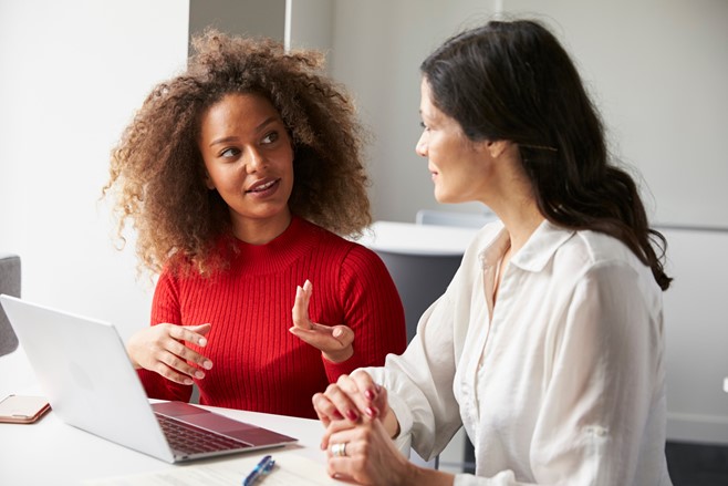 Two female workers in an office discussing about work using laptop