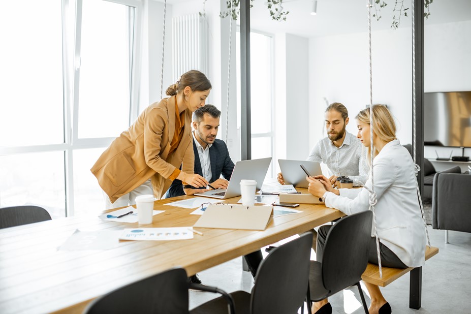 Four people working together in a modern office while using laptops and mobile device