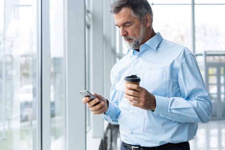Mature business owner acessing timetracking data report on his phone while having coffee