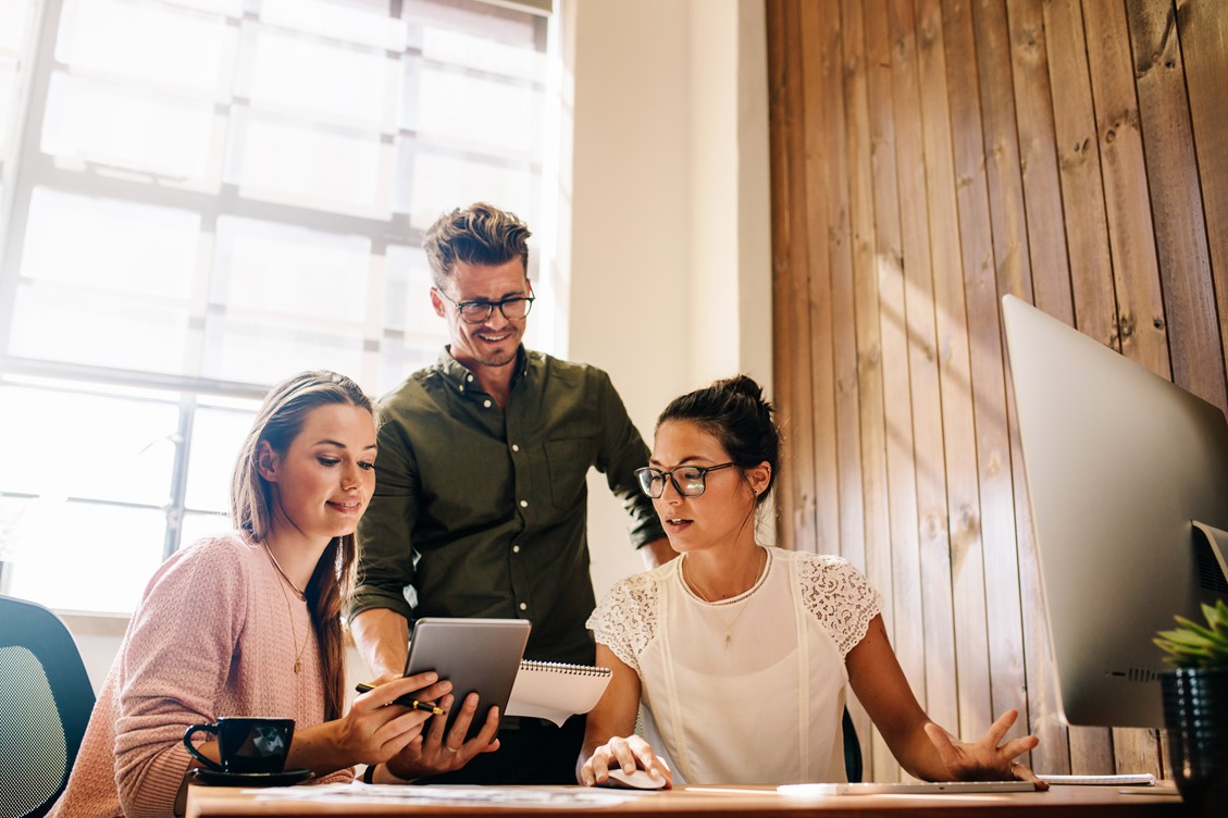 Three workmates looking at a tablet in an office while collaborating