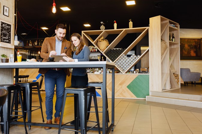 Two people standing while working at a cafe using a laptop