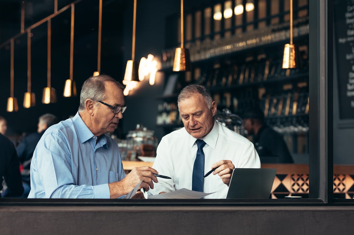 Two business men working at a cafe while looking at the printed copy of reporting analytics data
