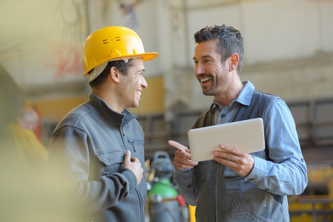 A boss holding a tablet and an employee smiling and working together harmoniously
